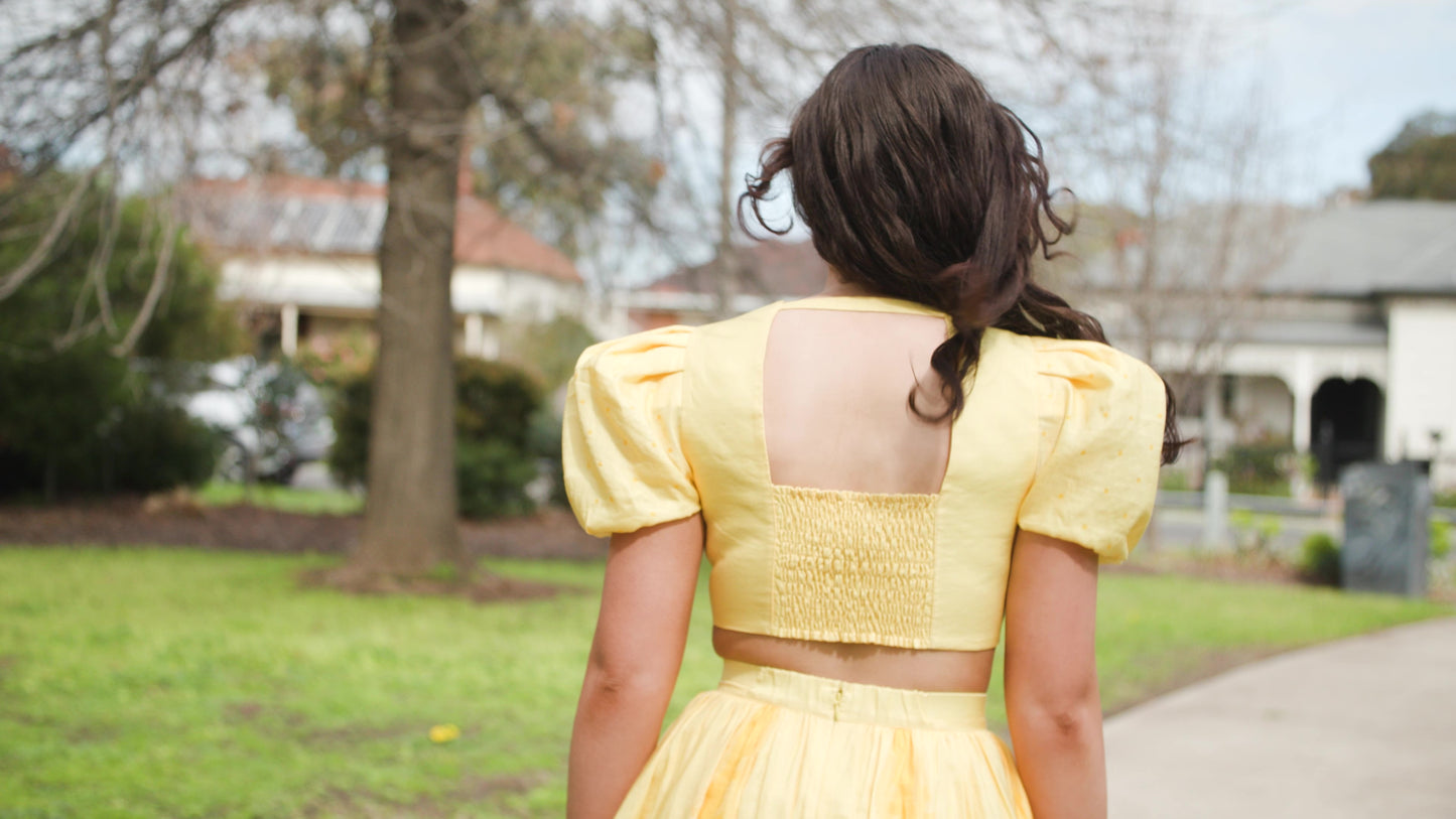 PRODUCT DESCRIPTION   Premium silk cotton linen, Daffodil-Yellow unique 2-piece midi dress with short puff sleeves exclusive to MAZASHIE.  Sweetheart neck, crop top with shirred back and bra-cut detail.  Placement prints on the voluminous skirt and polka-dotted puff sleeves.  The elasticated skirt waistband makes a perfect fit.  The shirred back band makes a perfect fit.  Invisible back zip closure at skirt.  Side seam concealed pockets.  Hooks and eyes closure at front.